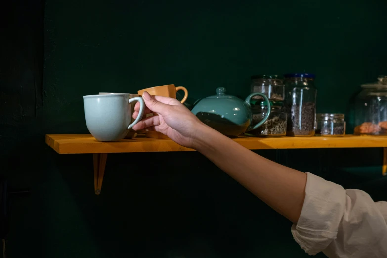 a close up of a person holding a cup on a shelf, teal studio backdrop, green tea, reaching out to each other, 15081959 21121991 01012000 4k