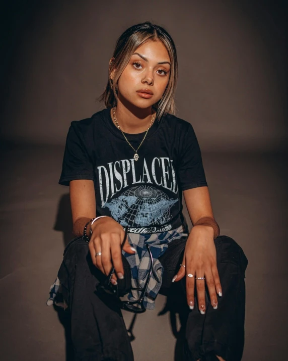 a woman sitting on the ground wearing a black shirt, an album cover, inspired by Elsa Bleda, trending on unsplash, plaid shirt, slightly dirty face, portrait of vanessa morgan, displacement