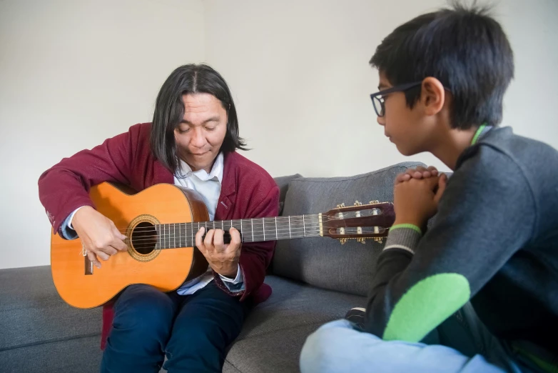 a person sitting on a couch playing a guitar, shin hanga, teaching, for junior, damien tran, compassionate