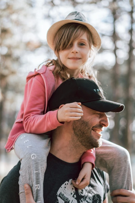 a man carrying a little girl on his shoulders, pexels contest winner, wearing a baseball hat, in front of a forest background, thumbnail, alexa grace