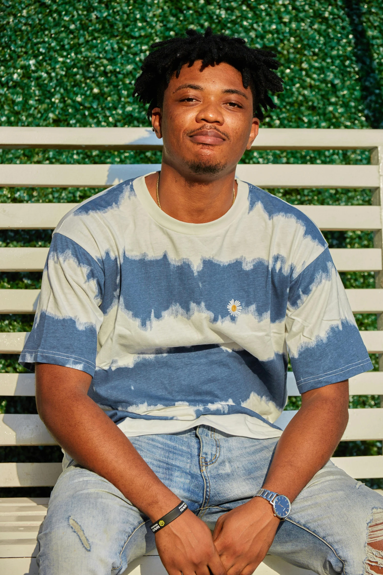 a man sitting on top of a white bench, wearing a tie-dye t-shirt, bluish and cream tones, in style of tyler mitchell, slide show