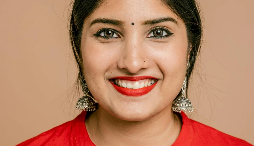 a close up of a person wearing a red shirt, by Julia Pishtar, trending on pexels, hurufiyya, indian girl with brown skin, smiling soft vibrant lips, traditional makeup, porcelain skin ”