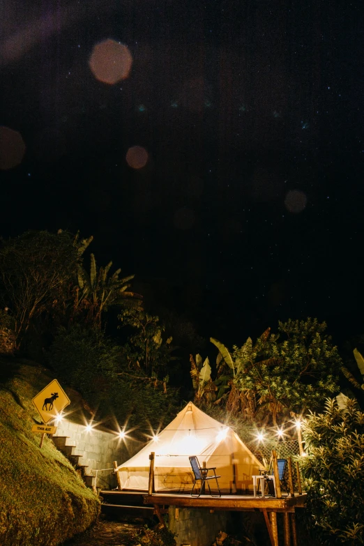 a couple of tents sitting on top of a lush green hillside, a portrait, by Jessie Algie, unsplash, party lights, tropical lighting, shot from above, low detail