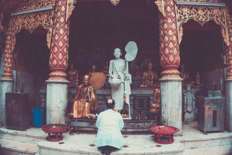 a person kneeling in front of a statue, pexels contest winner, buddhist temple, vintage color, white, colorful scene