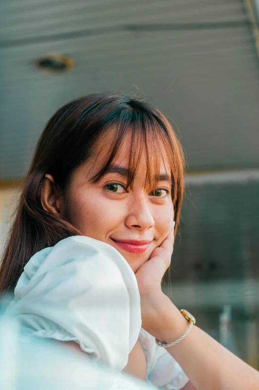 a woman sitting at a table with her hand on her chin, inspired by Ruth Jên, pexels contest winner, south east asian with round face, portrait of happy a young woman, center parted bangs, high angle closeup portrait