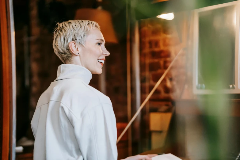 a woman standing in front of a laptop computer, by Lee Loughridge, pexels contest winner, white short hair, smiling at each other, leaning on door, standing in a restaurant