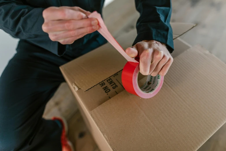 a man sitting on top of a cardboard box holding a pink tape, pexels contest winner, it has a red and black paint, inspect in inventory image, 40mm tape, with a sleek spoiler