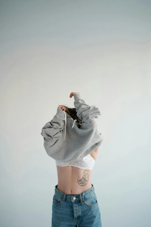 a woman standing with her back to the camera, a tattoo, by Emily Shanks, trending on pexels, hyperrealism, grey hoodie, shrugging, bralette, on a pale background