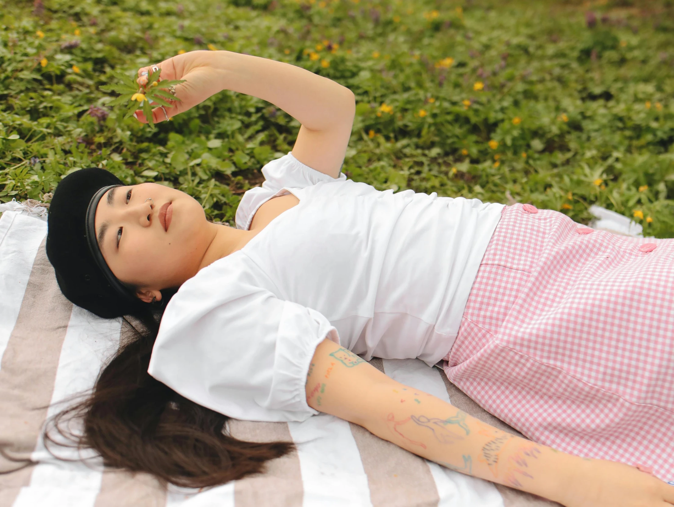 a woman laying on a blanket in the grass, inspired by Ren Hang, unsplash, magic realism, tattoo sleeve on her right arm, mukbang, cosplay photo, dressed in a white t shirt