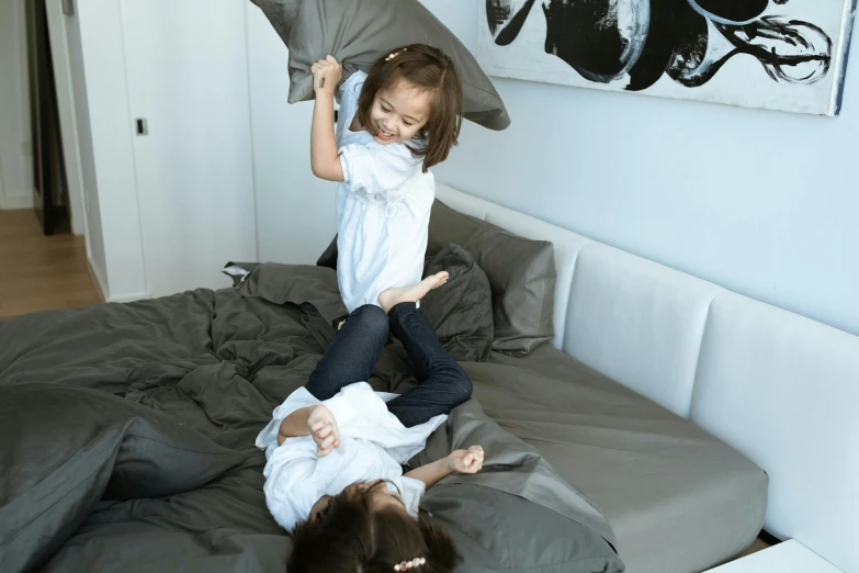 a couple of kids laying on top of a bed, by Tom Bonson, pexels contest winner, majestic sweeping action, grey, cushions, joy ang