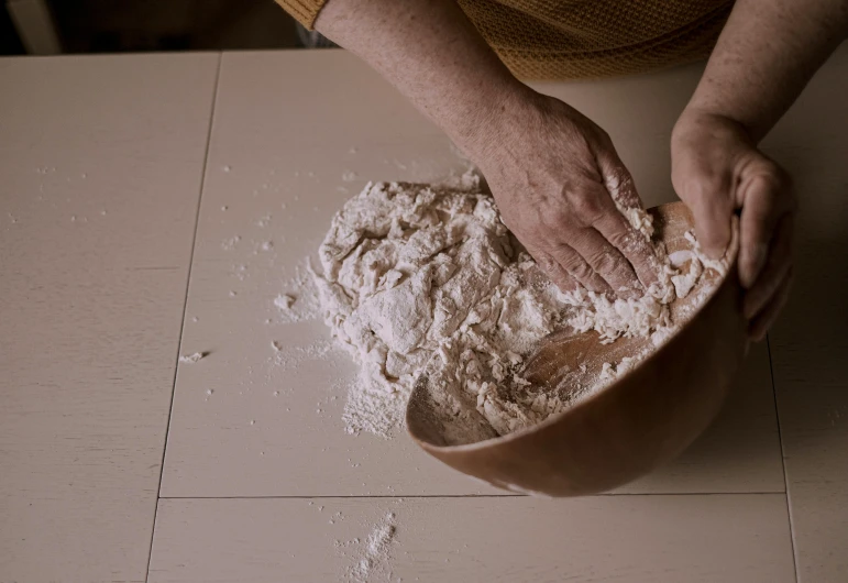 a person kneads flour in a bowl on a counter, by Elsa Bleda, trending on unsplash, fan favorite, carving, cardboard, background image