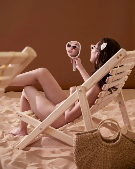 a woman sitting on a beach chair holding a mirror, unsplash, figuration libre, silicone skin, made of wood, fully posable, her skin is light brown