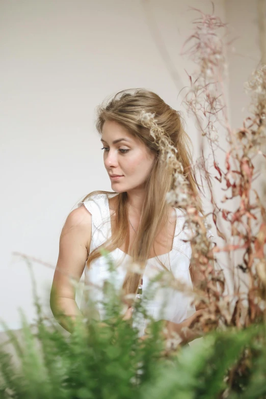 a woman standing in front of a bunch of flowers, by Alice Mason, trending on unsplash, renaissance, long braided hair pulled back, in a white boho style studio, branches sprouting from her head, wedding