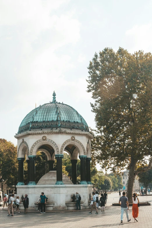 a group of people walking around a park, a statue, by Adam Szentpétery, trending on unsplash, art nouveau, rounded roof, ottoman sultan, well shaded, seen from outside