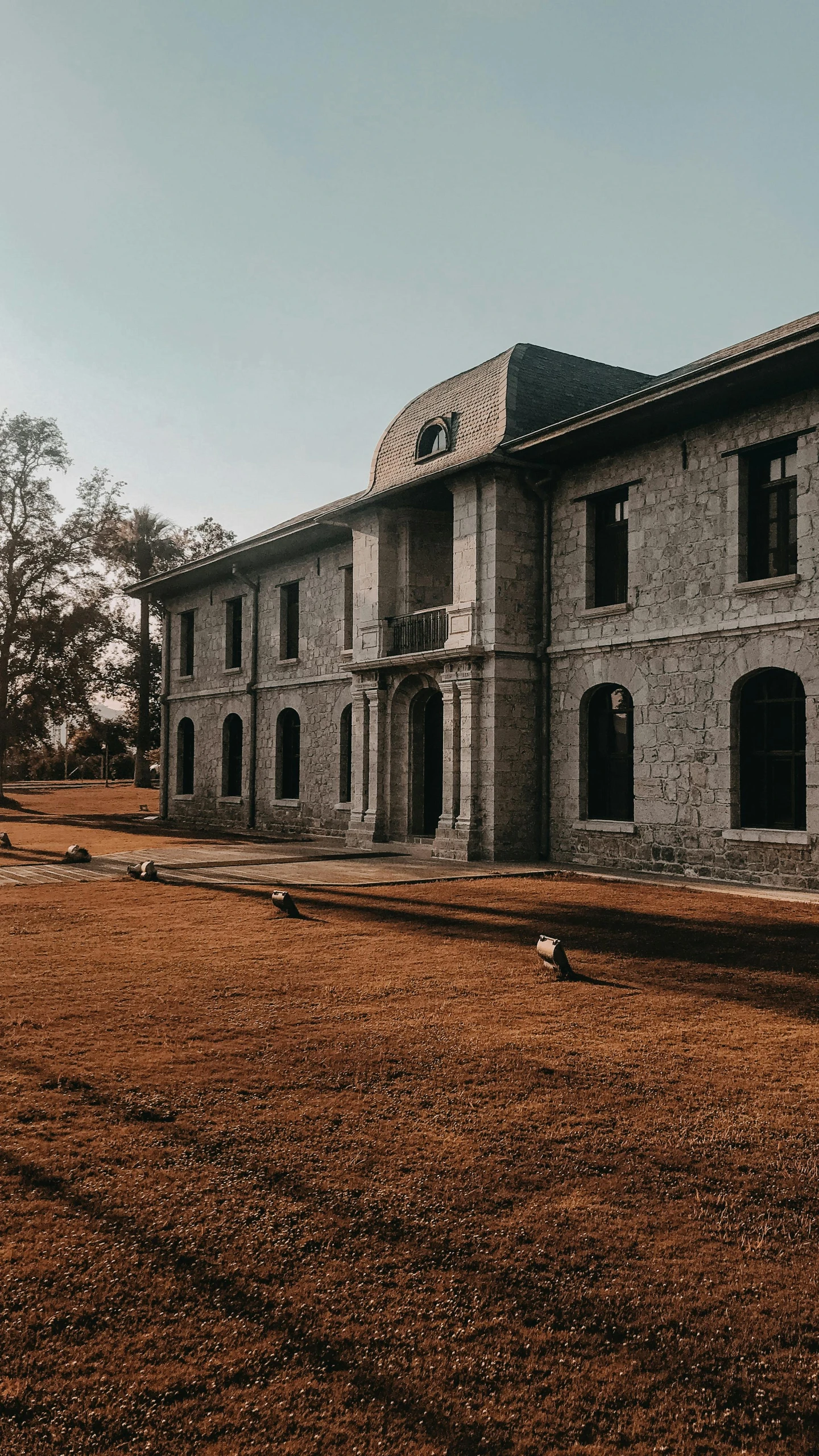 a large brick building sitting on top of a grass covered field, by Byron Galvez, pexels contest winner, bengal school of art, peaceful wooden mansion, front elevation view, creepy mood, celebration