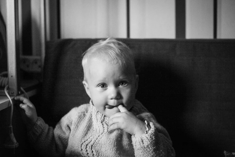 a black and white photo of a baby sitting on a couch, by Jaakko Mattila, unsplash, realism, smile 1950s, wearing a sweater, portrait shot 8 k, medium format. soft light