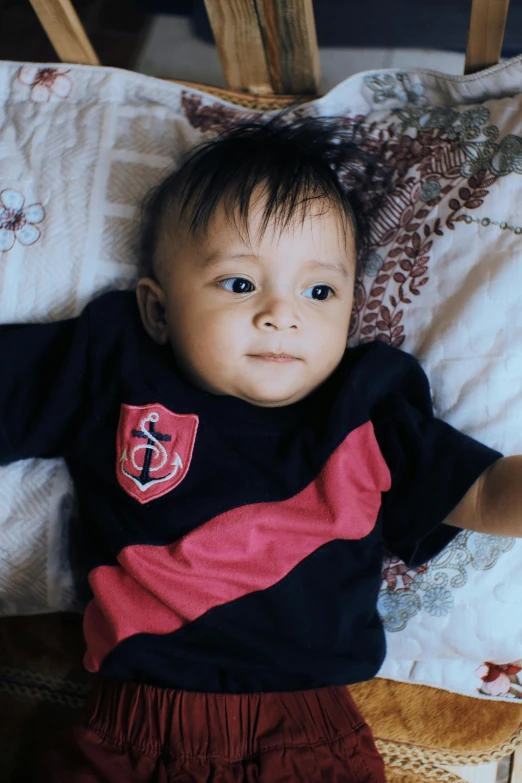 a small child laying on top of a bed, by Basuki Abdullah, symbolism, wearing dark maritime clothing, in red and black, wearing a t-shirt, medium close-up shot