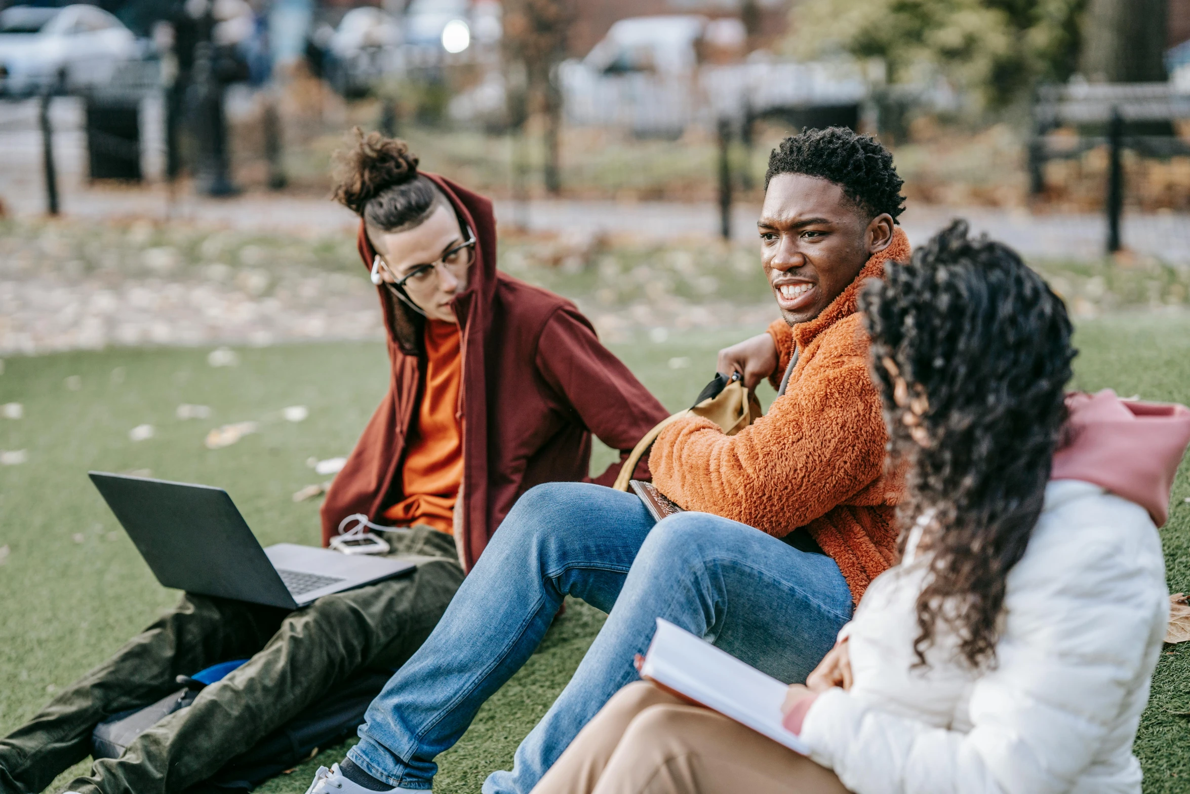 a group of people sitting on top of a grass covered field, by Carey Morris, trending on pexels, happening, trying to study, teal and orange colours, young man in a purple hoodie, in a city park