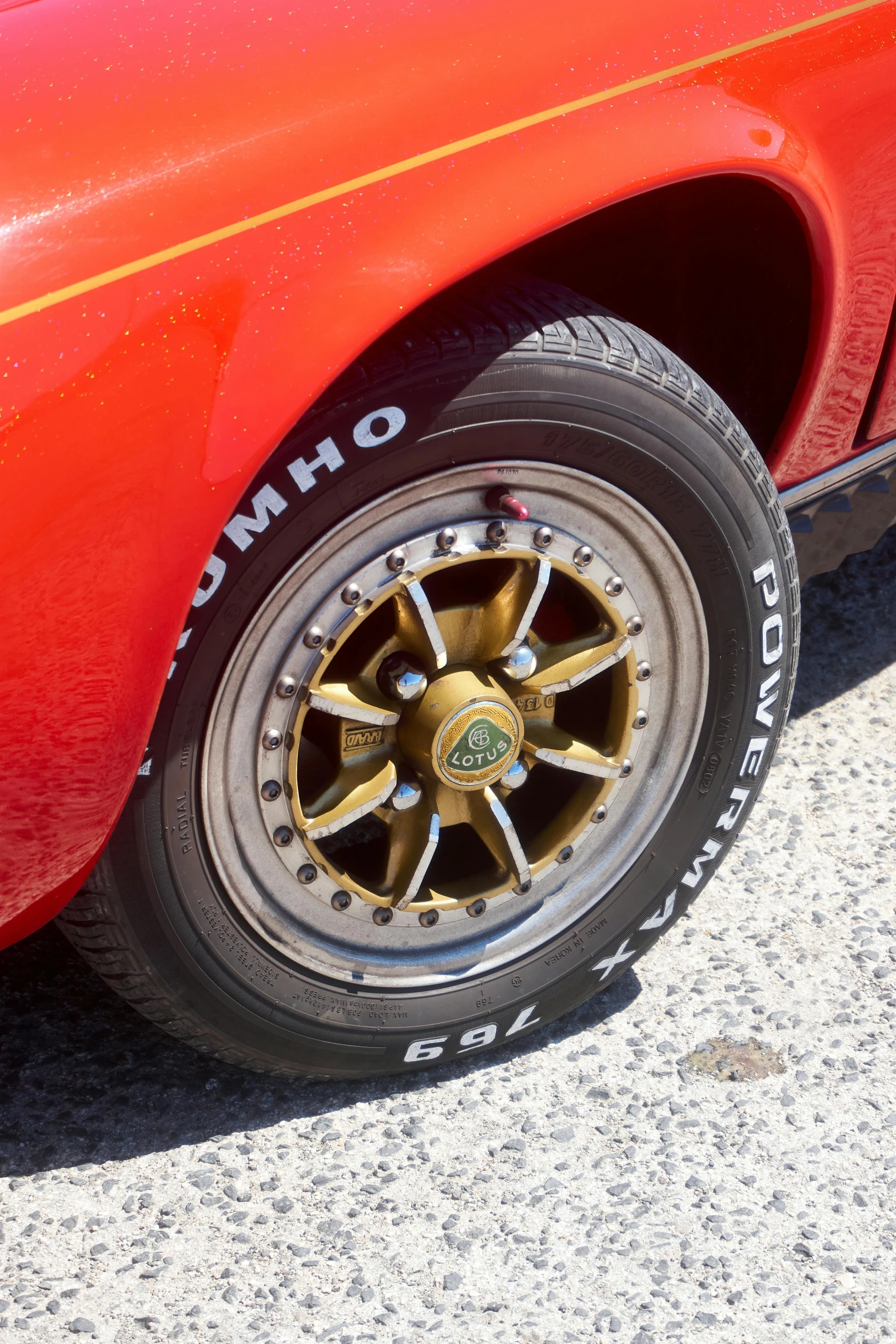 a red car parked on the side of the road, brass wheels, red white and gold color scheme, zoomed in, wikimedia commons