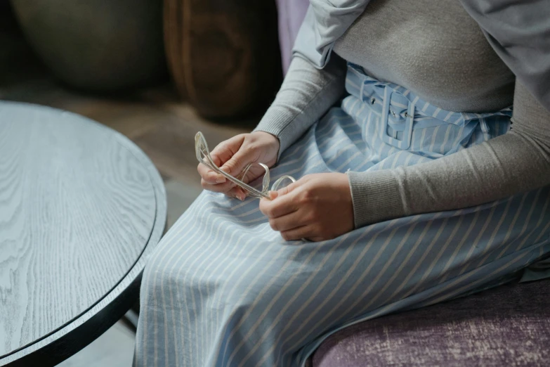 a woman sitting on a couch holding a glass, inspired by Elsa Beskow, trending on pexels, happening, square rimmed glasses, grey skirt, carefully crafted, striped