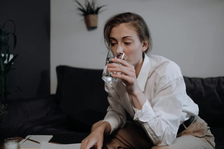 a woman sitting on a couch drinking a glass of water, pexels contest winner, hyperrealism, androgynous male, people at work, profile image, on a table