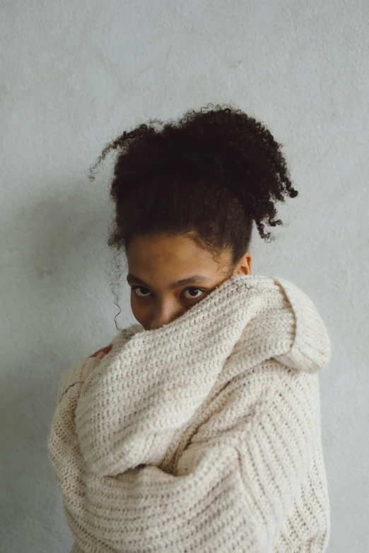 a close up of a person wrapped in a blanket, an album cover, by Lily Delissa Joseph, pexels contest winner, wearing a white sweater, girl with messy bun hairstyle, confident pose, mixed race