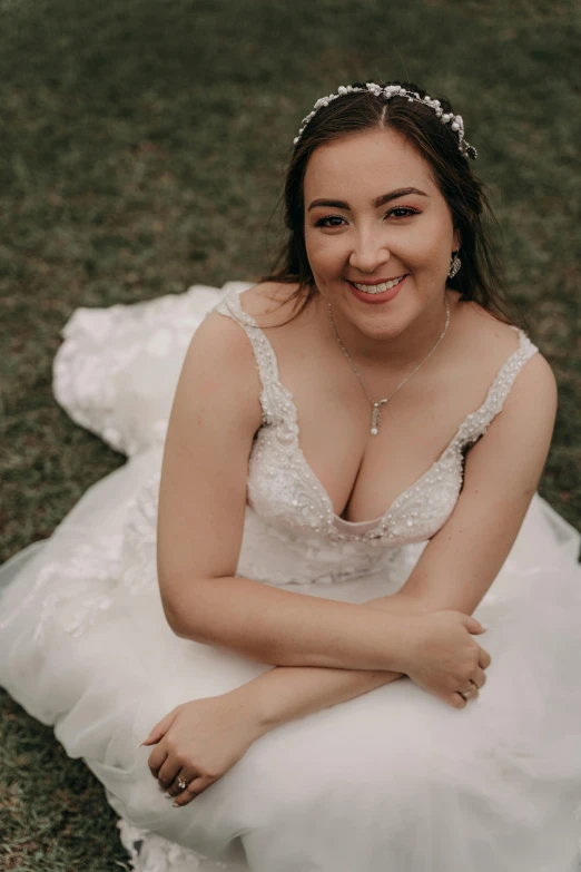 a woman sitting on top of a lush green field, wearing a wedding dress, happily smiling at the camera, straya, featured face details