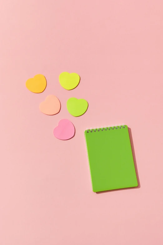 a green notepad sitting on top of a pink surface, several hearts, chartreuse color scheme, ((neon colors)), product shot