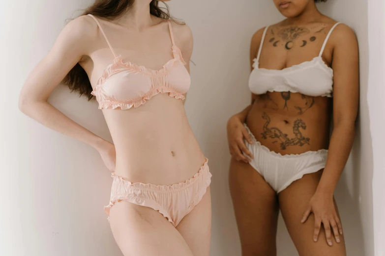 two women in underwear standing next to each other, trending on pexels, extremely pale, white and pink, white and black clothing, stomach skin