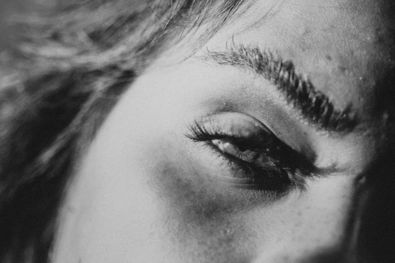 a black and white photo of a woman's eye, by Emma Andijewska, pexels, looking tired, eyebrow scar, eyes closed, realistic picture