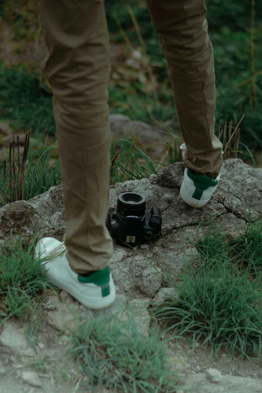 a person standing on a rock with a camera, with an ashtray on top, green legs, wearing white sneakers, petzval lens
