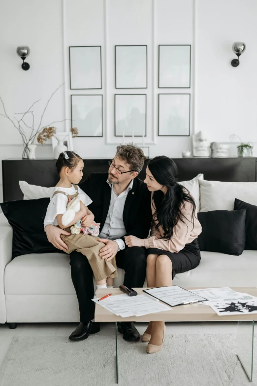 a man and woman sitting on a couch with a child, in a white room, white and black color palette, on a table, ceo