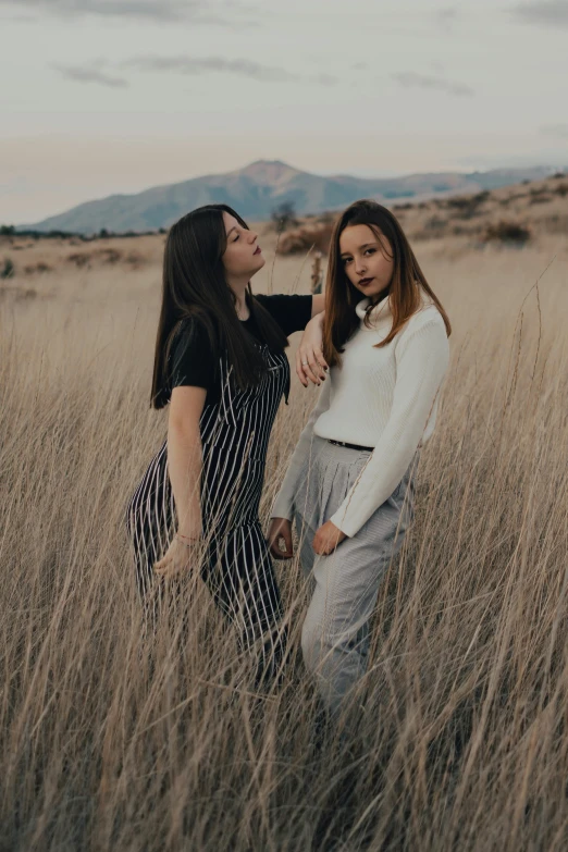 two women standing in a field of tall grass, trending on pexels, teen, casual pose, mountainside, grey