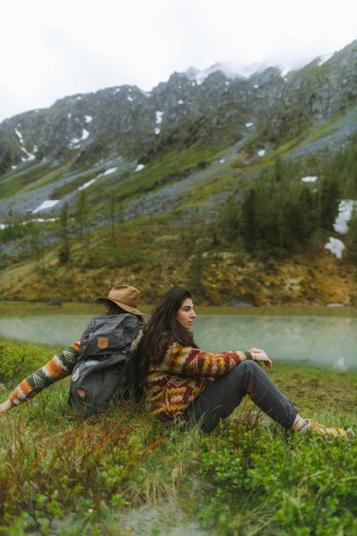 a couple of people that are sitting in the grass, traveling through the mountains, standing next to water, profile image, trending photo