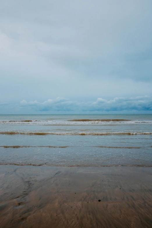 a man riding a surfboard on top of a sandy beach, unsplash, minimalism, omaha beach, on a cloudy day, today\'s featured photograph 4k, muted color (blues