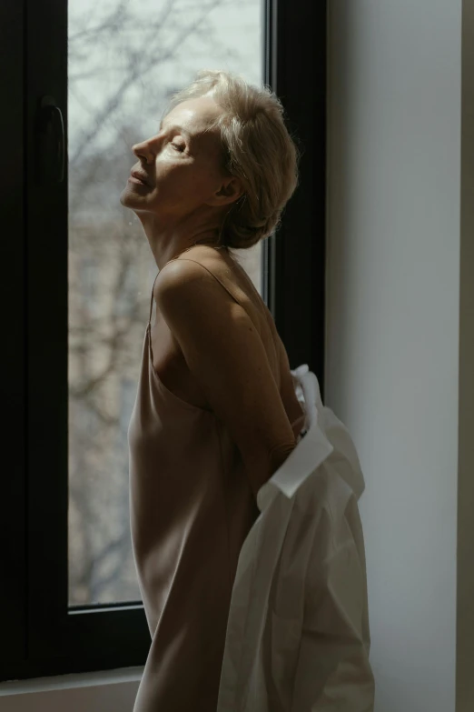 a woman standing in front of a window, inspired by Nan Goldin, unsplash, renaissance, wearing a towel, soft light.4k, cate blanchet, wearing translucent sheet