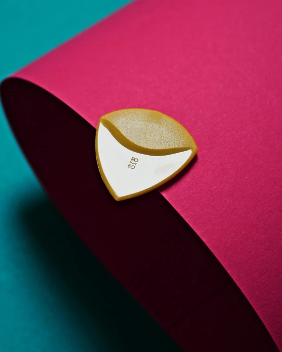 a cookie sitting on top of a pink paper, inspired by Lucio Fontana, private press, sharp metal crest, material design, detail shot, curved