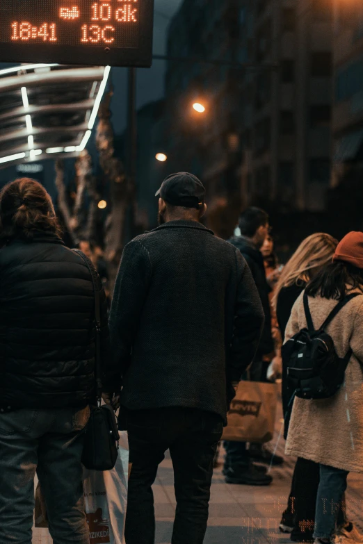 a group of people standing next to each other on a sidewalk, by Niko Henrichon, pexels contest winner, happening, city street lights, a man wearing a black jacket, customers, with his back turned