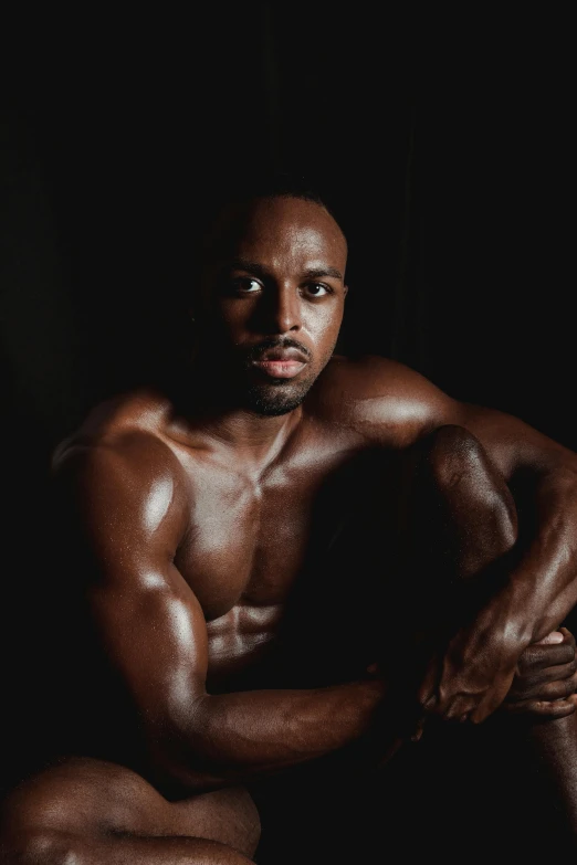 a man sitting in front of a black background, inspired by Leonard Daniels, pexels contest winner, muscular men entwined together, black skin, mesomorph, confident looking