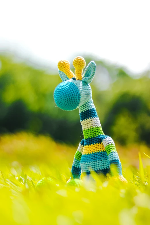 a stuffed giraffe sitting on top of a lush green field, bright colour, crochet, sky blue, zoomed in