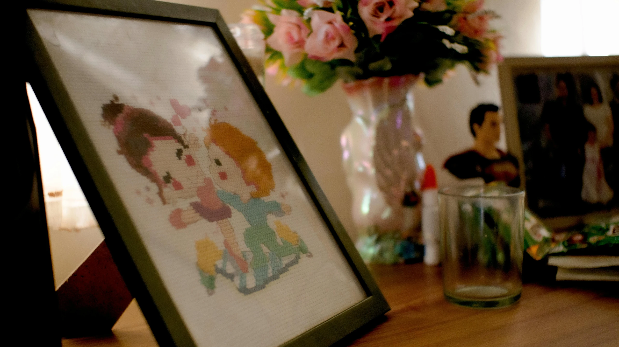 a picture frame sitting on top of a wooden table, a cross stitch, by Petr Brandl, pexels, betty boop, bouquet, low quality footage, promo image