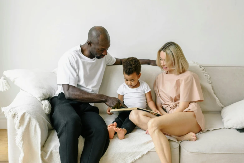 a man and woman sitting on a couch with a child, pexels contest winner, brown and cream color scheme, trying to read, black man, slightly minimal