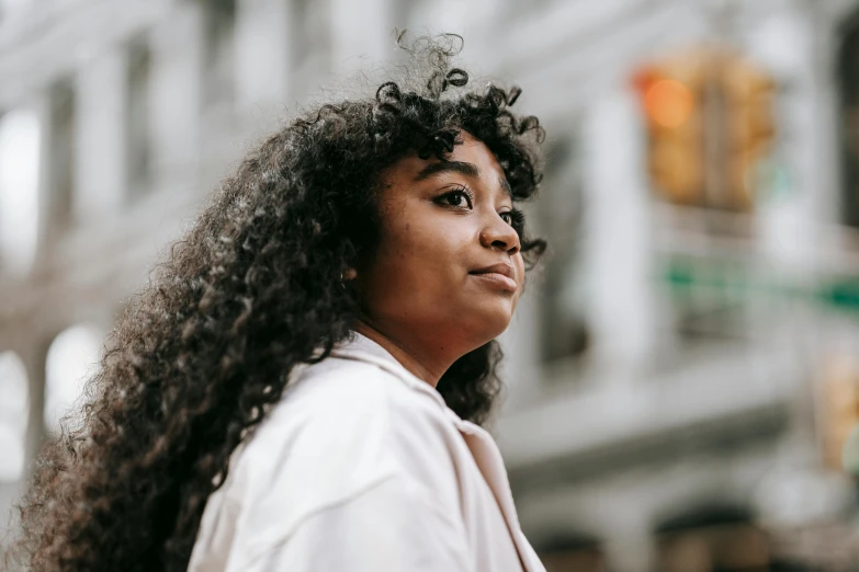 a woman with long curly hair standing in front of a building, pexels contest winner, black teenage girl, looking off into the distance, wearing a white button up shirt, essence