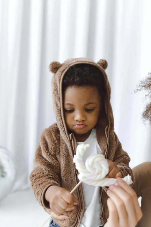 a woman holding a child in a bear costume, pexels, marshmallows, beige hoodie, ( ( dark skin ) ), concentration