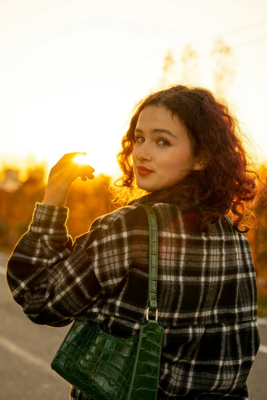 a woman standing on the side of a road holding a green purse, by Sven Erixson, pexels contest winner, sunset backlight, wearing a flannel shirt, curly haired, teenage girl