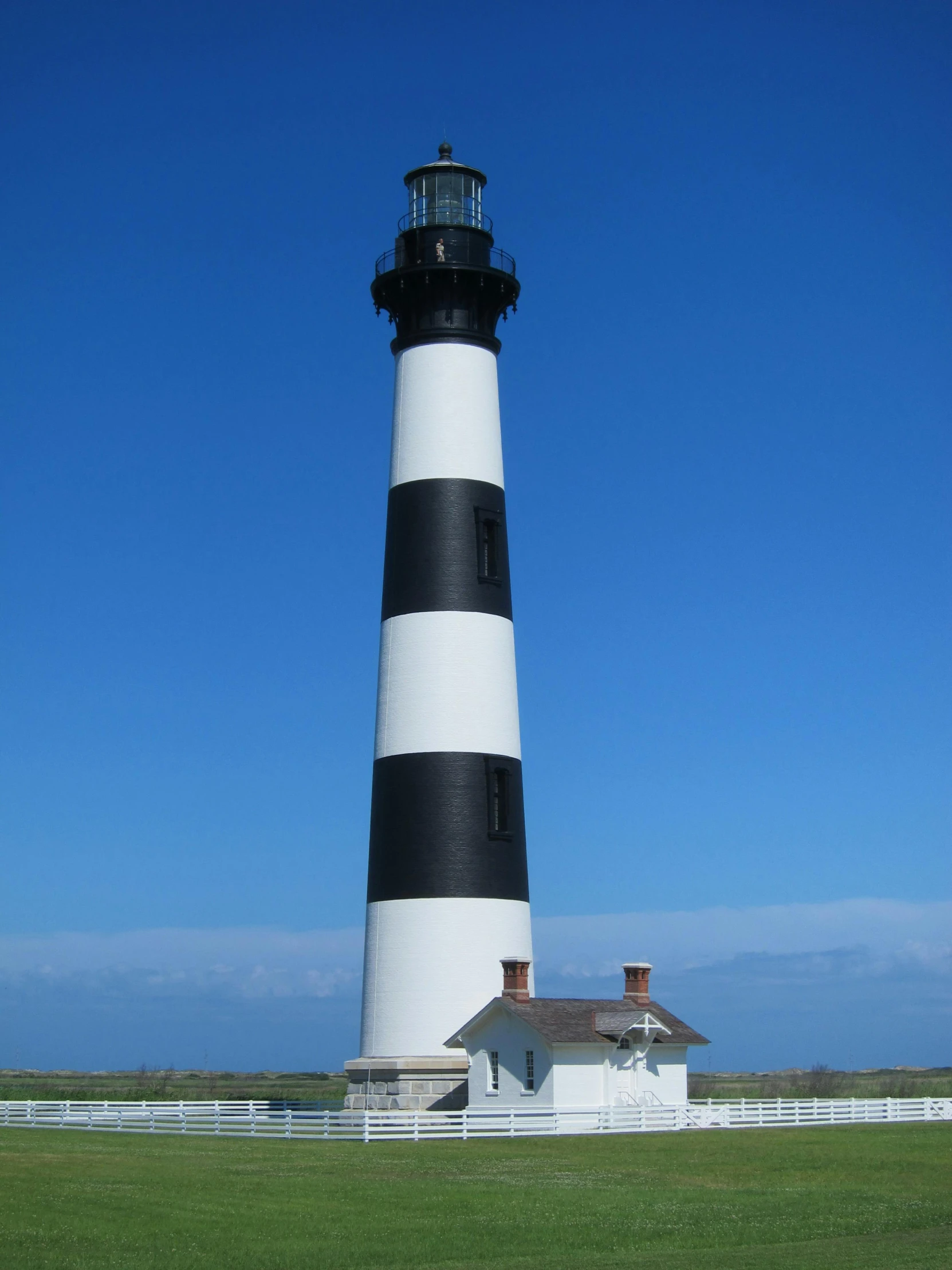 a black and white lighthouse sitting on top of a lush green field, tall columns, profile picture, built around ocean, chimneys