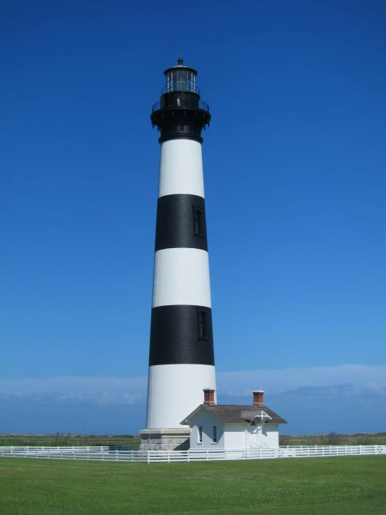 a black and white lighthouse sitting on top of a lush green field, tall columns, profile picture, built around ocean, chimneys