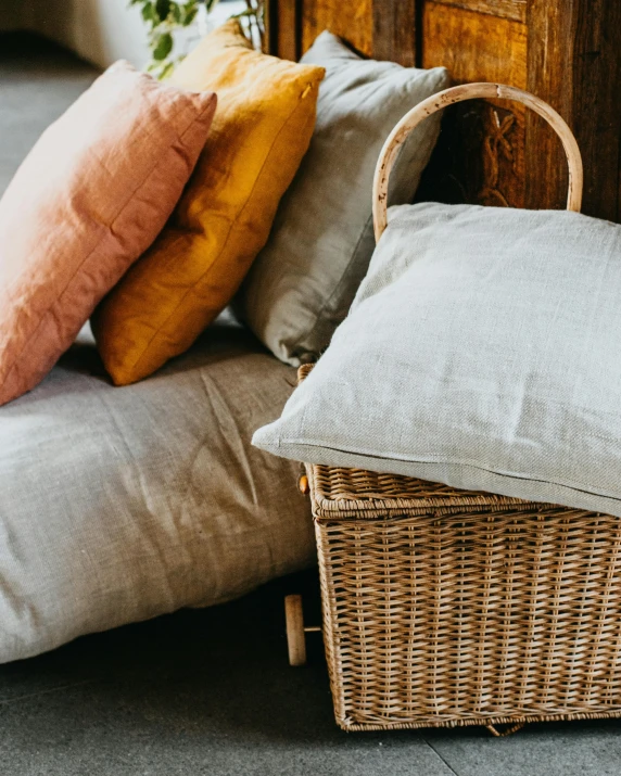 a wicker basket sitting on top of a floor next to pillows, unsplash, close-up product photo