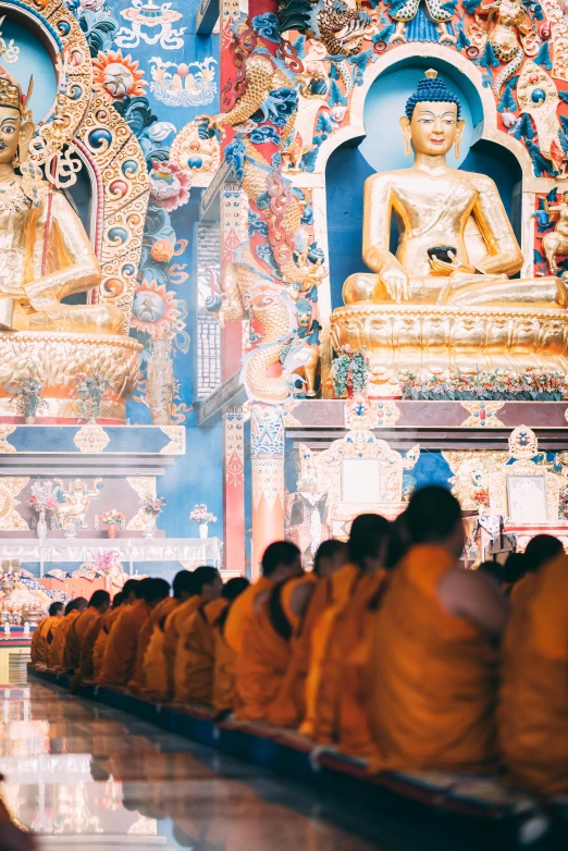 a group of people that are sitting in a room, in a temple, yellow robe, facing away from the camera, buddhism