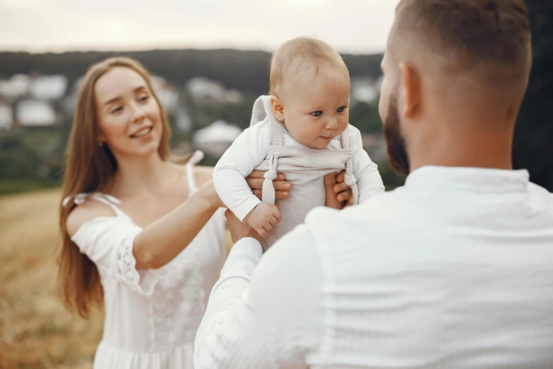a man holding a baby in his arms, pexels contest winner, wearing white clothes, parents watching, avatar image, cute woman